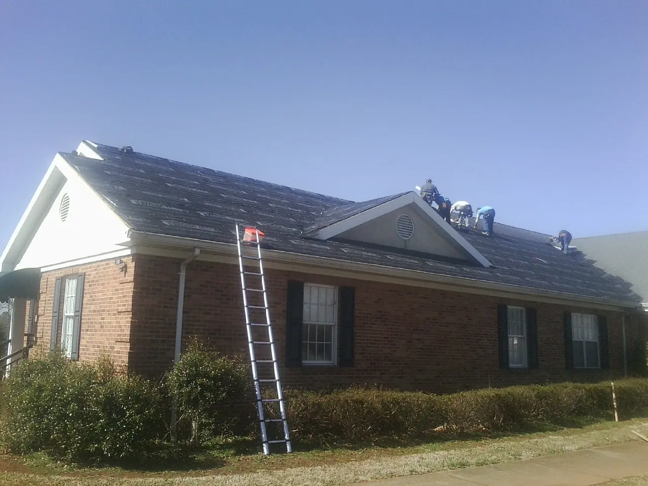 Crew tearing shingles off a brick ranch roof with a ladder set — Emergency Roof Repair work by our crew in Peyton