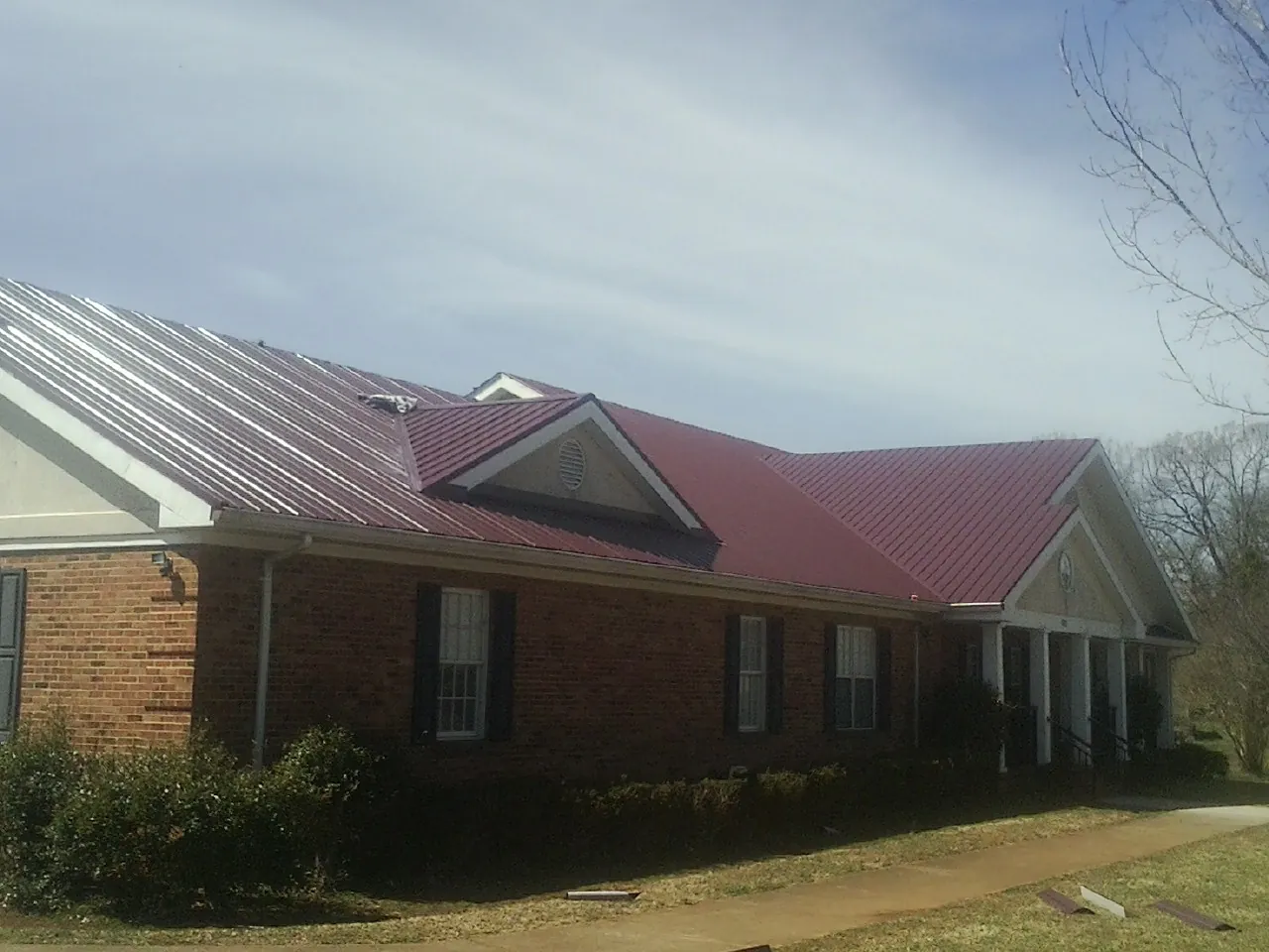 Red metal roof with gabled entries on a long brick building, from a Hail Damage Roof Repair job in Peyton