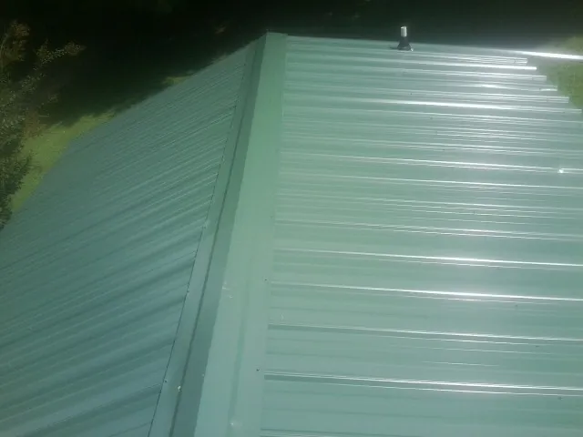 New green metal panels meeting at the ridge of a roof — Flat Roof Repair work by our crew in Peyton