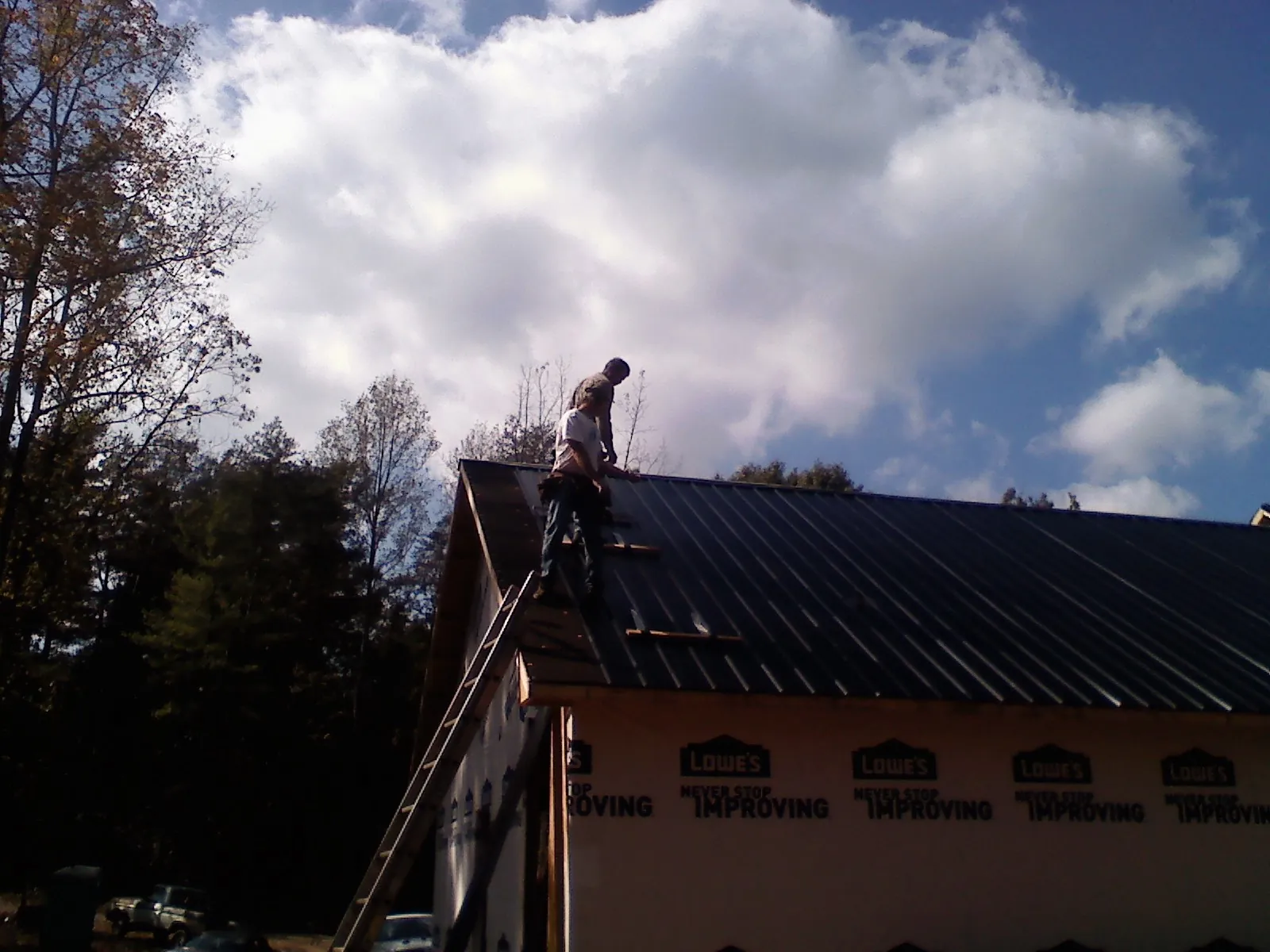 Roofer fastening dark metal panels high against a cloudy sky, from a Roof Inspection job in Peyton