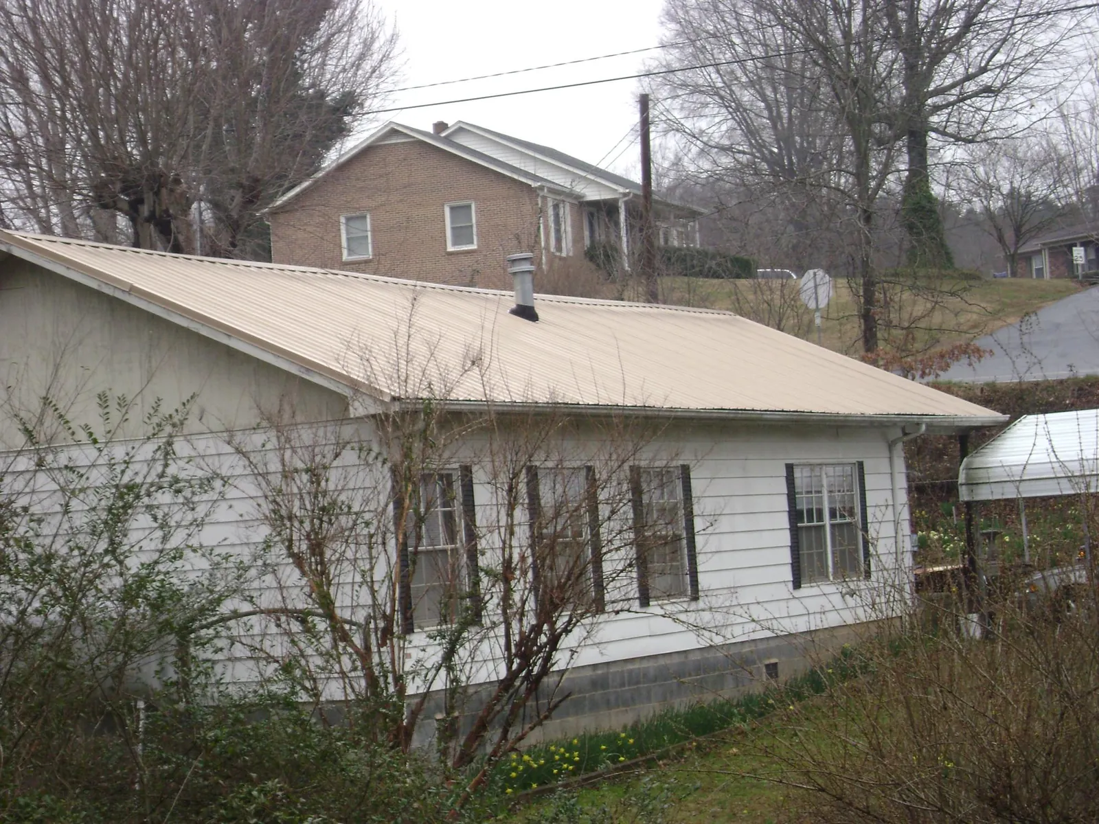 Tan metal roof on a white sided house set into a hillside — Commercial Roofing by Roofing Brothers in Peyton